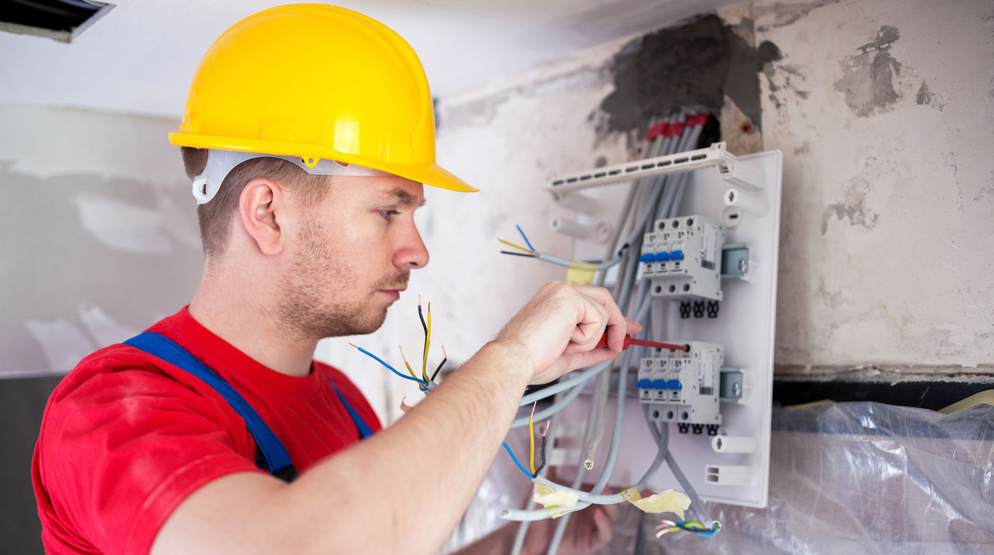 Vue de profil d'un électricien en action tirant des câbles électriques à travers une gaine pendant des travaux de rénovation dans un espace lumineux