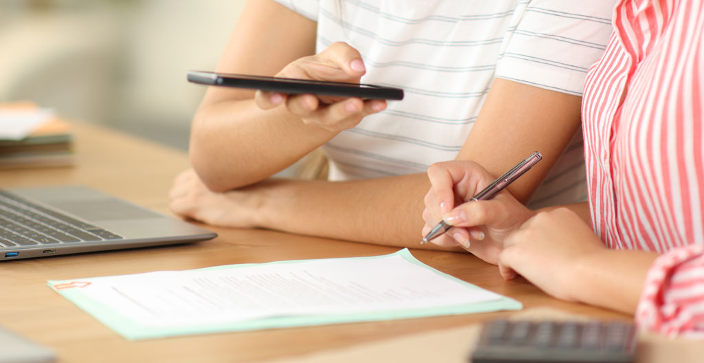 Gros plan sur des mains tenant un stylo au-dessus d'un avec une calculatrice et des factures sur un bureau lumineux