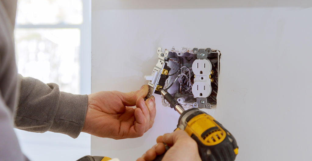 Main d'électricien vue de profil utilisant un testeur de tension sur une prise murale dans un intérieur moderne